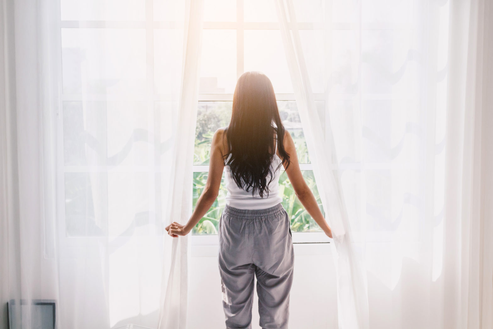 Woman holding drapes looking out window