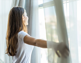 Woman holding drapes looking out window