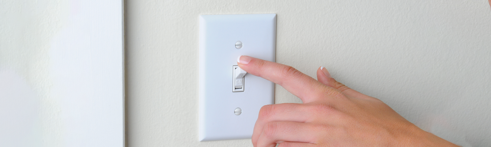 Hand turning off light switch to conserve energy